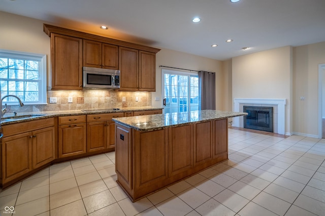 kitchen featuring brown cabinetry, a sink, stainless steel microwave, tasteful backsplash, and a center island