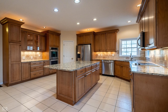 kitchen featuring a kitchen island, light tile patterned floors, light stone counters, appliances with stainless steel finishes, and a sink