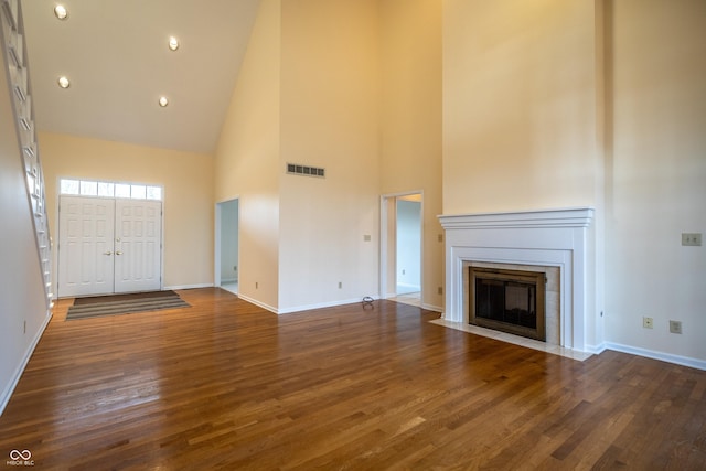 unfurnished living room with visible vents, baseboards, a fireplace with flush hearth, wood finished floors, and high vaulted ceiling