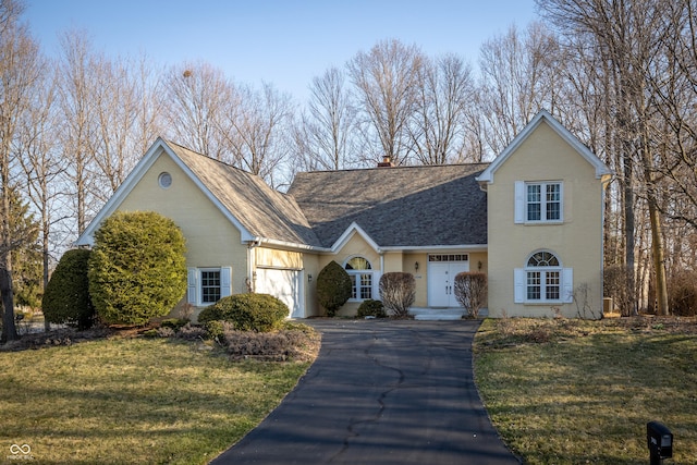 traditional-style home featuring roof with shingles, a front yard, a chimney, a garage, and driveway