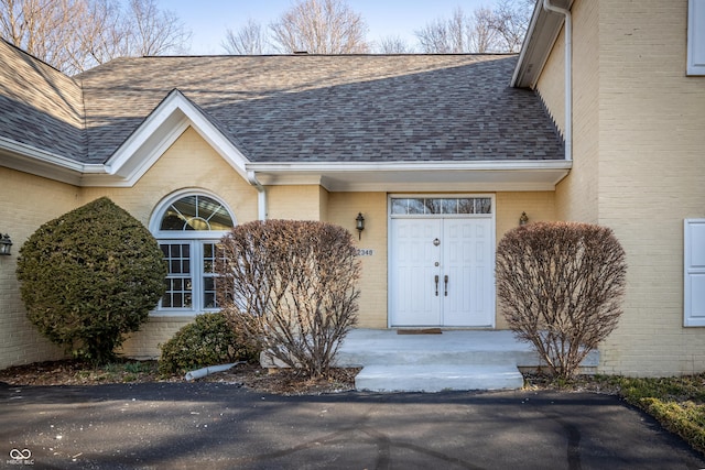 view of exterior entry featuring brick siding and a shingled roof