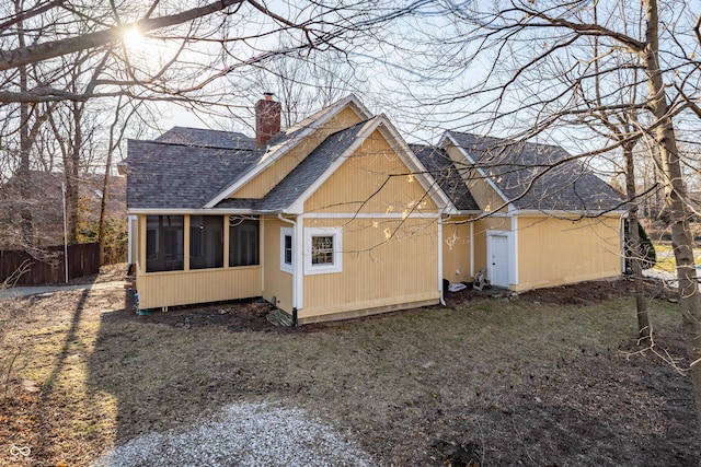 rear view of house featuring fence, a chimney, a sunroom, and a shingled roof