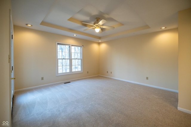 empty room featuring a tray ceiling, baseboards, visible vents, and ceiling fan