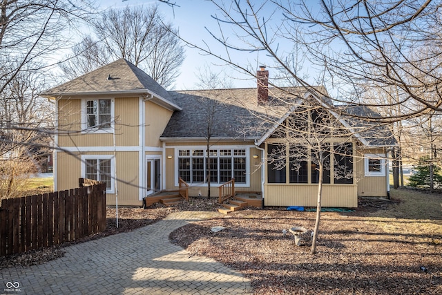 back of house featuring entry steps, a shingled roof, fence, a sunroom, and a chimney