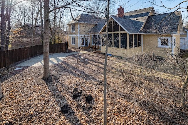 rear view of house featuring a chimney, a shingled roof, a sunroom, and fence