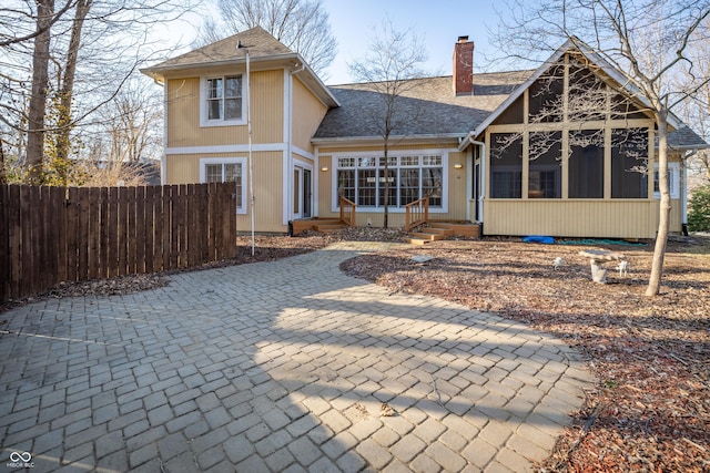 rear view of house with entry steps, fence, roof with shingles, a sunroom, and a chimney