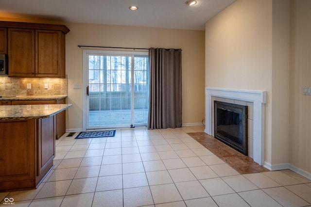 kitchen with light stone counters, brown cabinetry, light tile patterned flooring, decorative backsplash, and stainless steel microwave