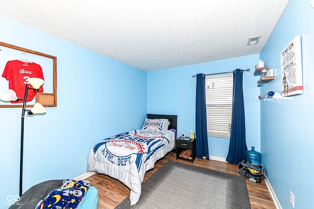 bedroom with visible vents, a textured ceiling, baseboards, and wood finished floors