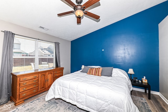 bedroom with visible vents, a textured ceiling, wood finished floors, baseboards, and ceiling fan