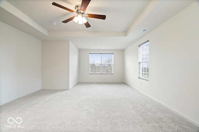 spare room with a raised ceiling, light colored carpet, and baseboards