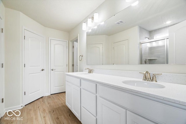 full bathroom featuring visible vents, a shower stall, wood finished floors, and a sink