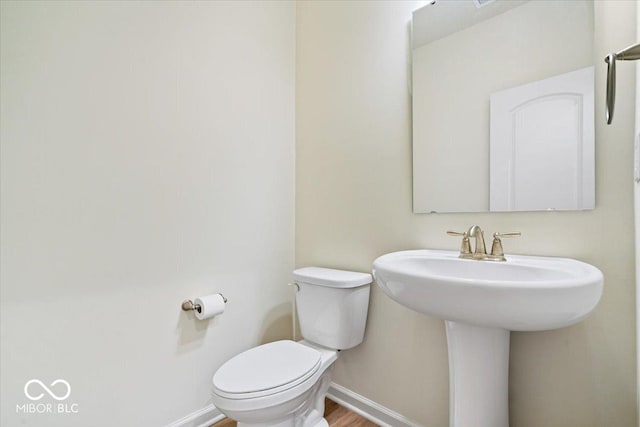 half bath featuring toilet, baseboards, and wood finished floors