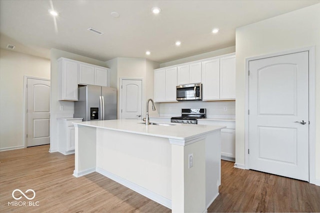 kitchen featuring visible vents, a center island with sink, a sink, white cabinetry, and appliances with stainless steel finishes