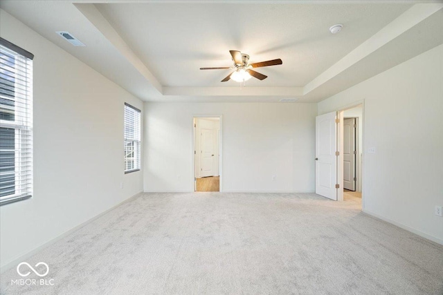 spare room featuring visible vents, light carpet, a ceiling fan, a tray ceiling, and baseboards