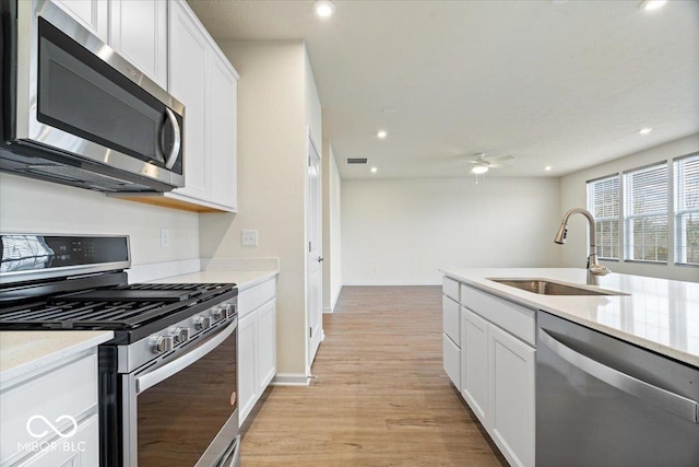 kitchen featuring light wood-style flooring, ceiling fan, a sink, white cabinets, and appliances with stainless steel finishes