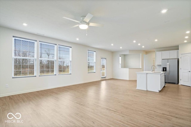 unfurnished living room featuring recessed lighting, light wood-style flooring, baseboards, and a sink