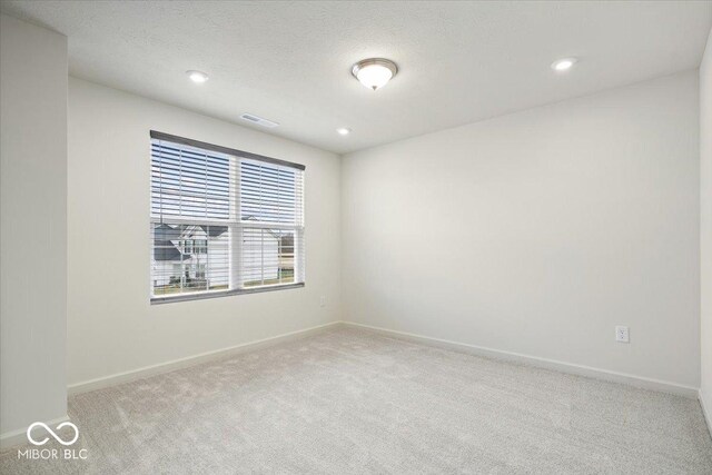 empty room with visible vents, light colored carpet, a textured ceiling, and baseboards