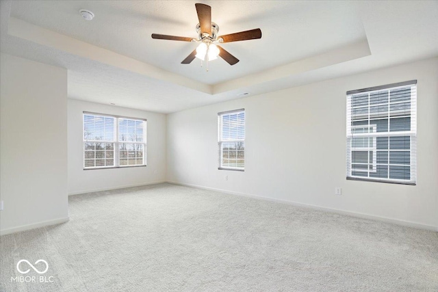 empty room with a tray ceiling, baseboards, a wealth of natural light, and light carpet