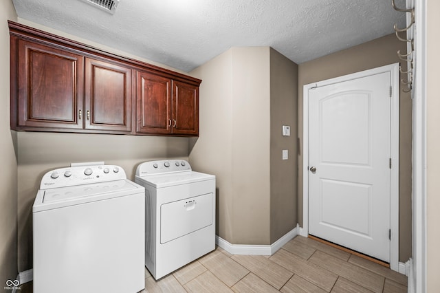 clothes washing area featuring visible vents, baseboards, cabinet space, a textured ceiling, and washer and dryer