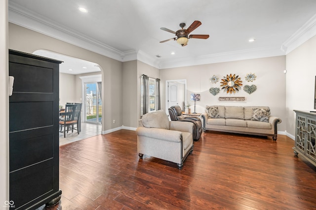 living area featuring wood finished floors, crown molding, a ceiling fan, and arched walkways