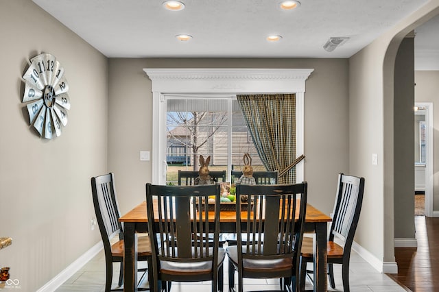 dining area featuring visible vents, light wood-style flooring, recessed lighting, arched walkways, and baseboards