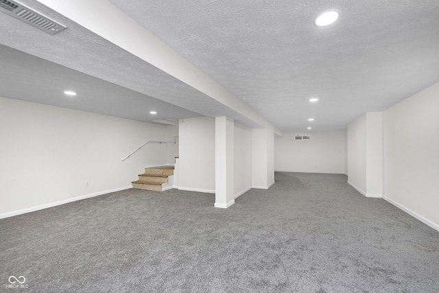 finished basement with stairway, carpet, baseboards, visible vents, and a textured ceiling