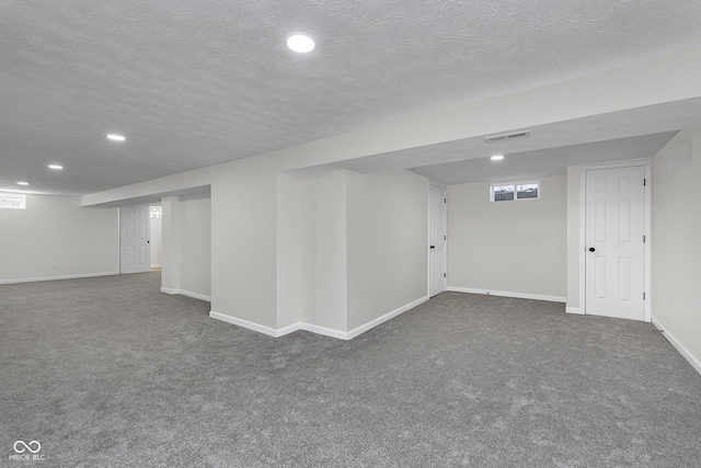 finished below grade area featuring visible vents, a textured ceiling, baseboards, and carpet