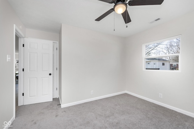 carpeted spare room featuring baseboards, visible vents, and ceiling fan