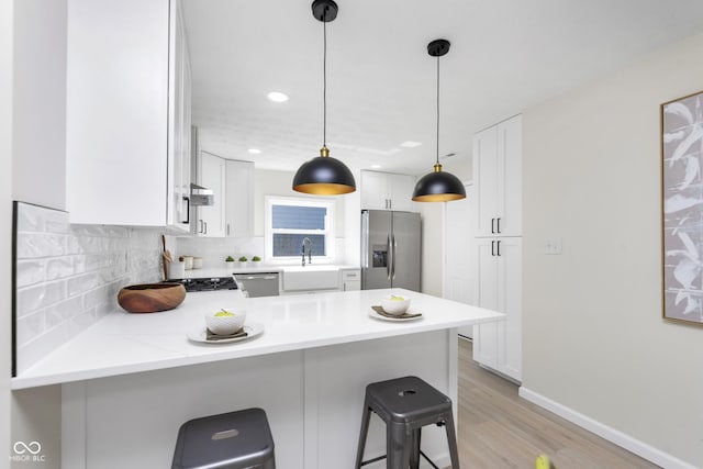 kitchen with a sink, backsplash, white cabinetry, stainless steel appliances, and a peninsula