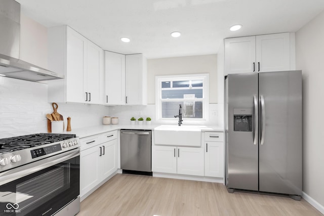 kitchen featuring white cabinetry, stainless steel appliances, wall chimney exhaust hood, and light countertops