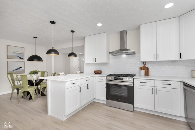 kitchen featuring backsplash, white cabinetry, stainless steel appliances, a peninsula, and wall chimney range hood