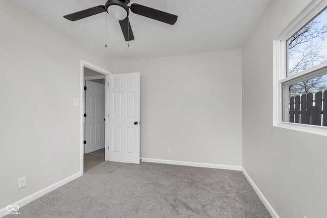 carpeted spare room with a ceiling fan and baseboards