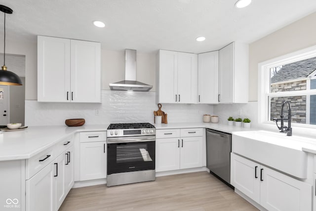 kitchen featuring a sink, stainless steel appliances, wall chimney exhaust hood, and light countertops