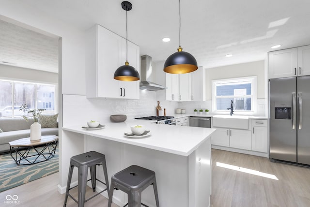 kitchen featuring a breakfast bar area, a sink, appliances with stainless steel finishes, wall chimney exhaust hood, and tasteful backsplash