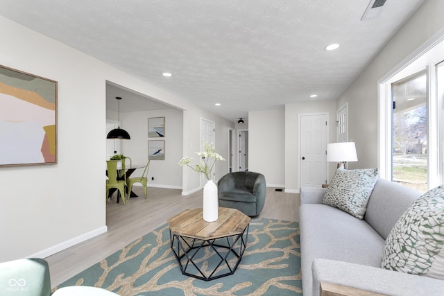 living area featuring visible vents, a textured ceiling, wood finished floors, recessed lighting, and baseboards