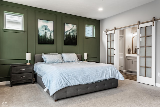 carpeted bedroom with a decorative wall, recessed lighting, ensuite bath, and a barn door