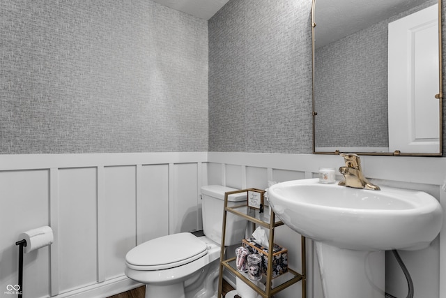 half bath featuring a decorative wall, toilet, and a wainscoted wall