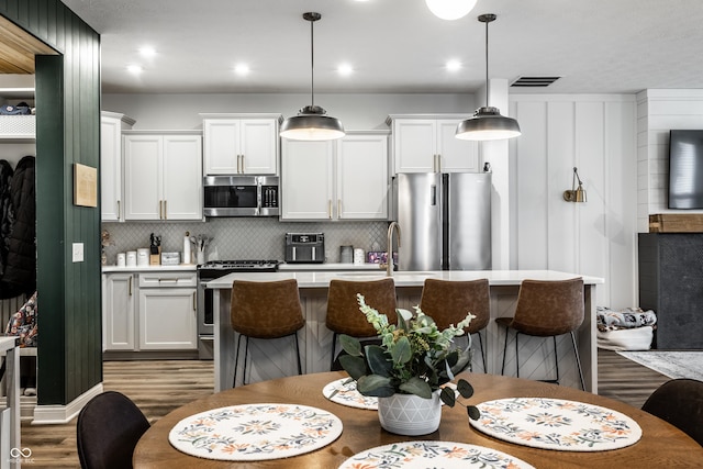 kitchen featuring wood finished floors, a kitchen island with sink, stainless steel appliances, light countertops, and a kitchen bar