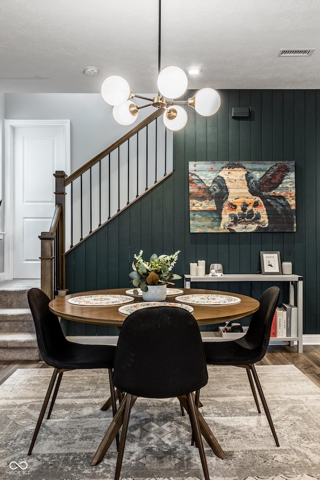 dining area with stairway, visible vents, an inviting chandelier, and wood finished floors