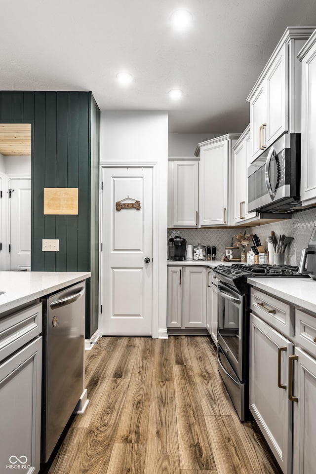 kitchen with wood finished floors, recessed lighting, stainless steel appliances, white cabinets, and decorative backsplash