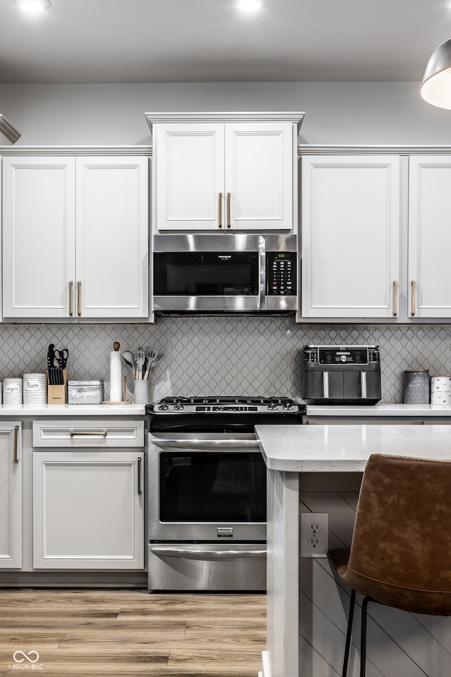 kitchen featuring decorative backsplash, white cabinets, stainless steel appliances, and light wood-type flooring