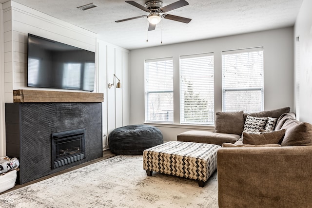 living room with visible vents, a tile fireplace, wood finished floors, a textured ceiling, and a ceiling fan