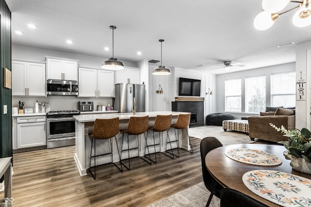 kitchen with open floor plan, a breakfast bar, light countertops, appliances with stainless steel finishes, and wood finished floors