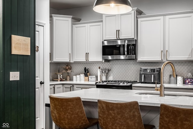 kitchen with a sink, stainless steel microwave, light stone counters, decorative backsplash, and range