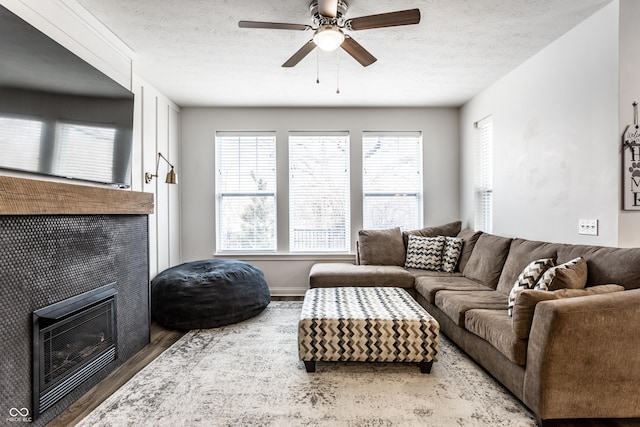 living room with wood finished floors, a textured ceiling, ceiling fan, and a tile fireplace