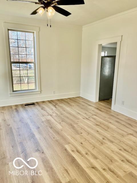 unfurnished room with light wood-type flooring, visible vents, ornamental molding, baseboards, and ceiling fan