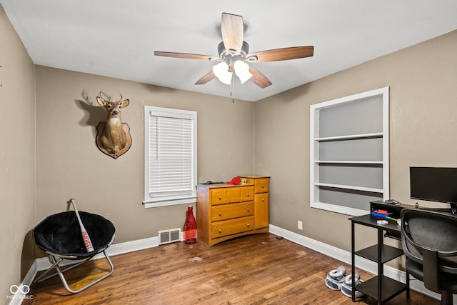 office area featuring visible vents, built in shelves, ceiling fan, baseboards, and dark wood finished floors