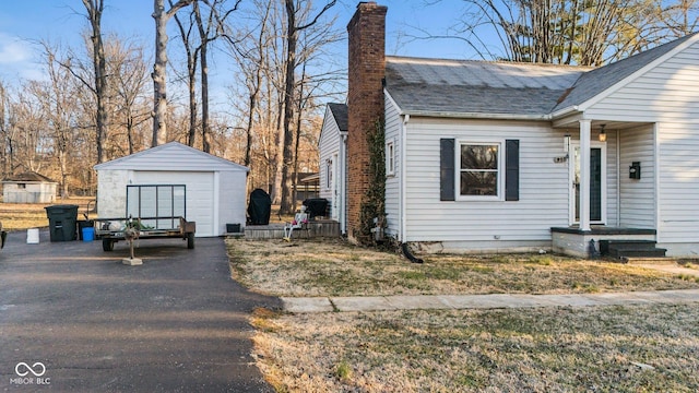 view of front of property featuring a chimney, a detached garage, an outdoor structure, and roof with shingles