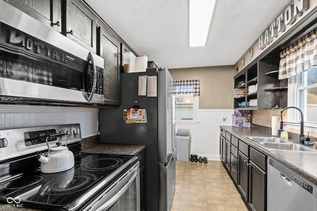 kitchen featuring a sink, open shelves, dark countertops, stainless steel appliances, and wainscoting