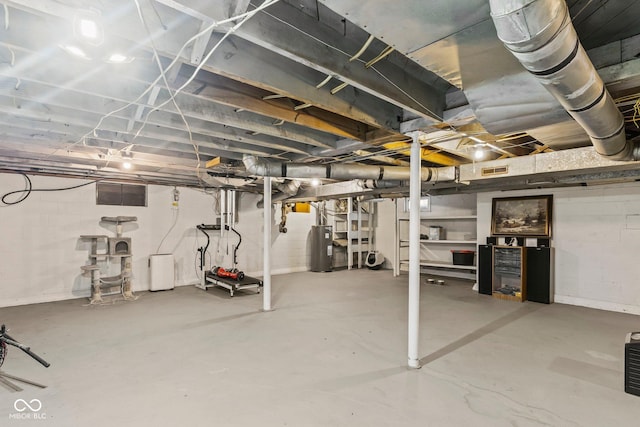 unfinished basement with water heater, visible vents, and concrete block wall